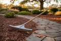 Realistic landscape rake resting on a mulch bed beside a stone path